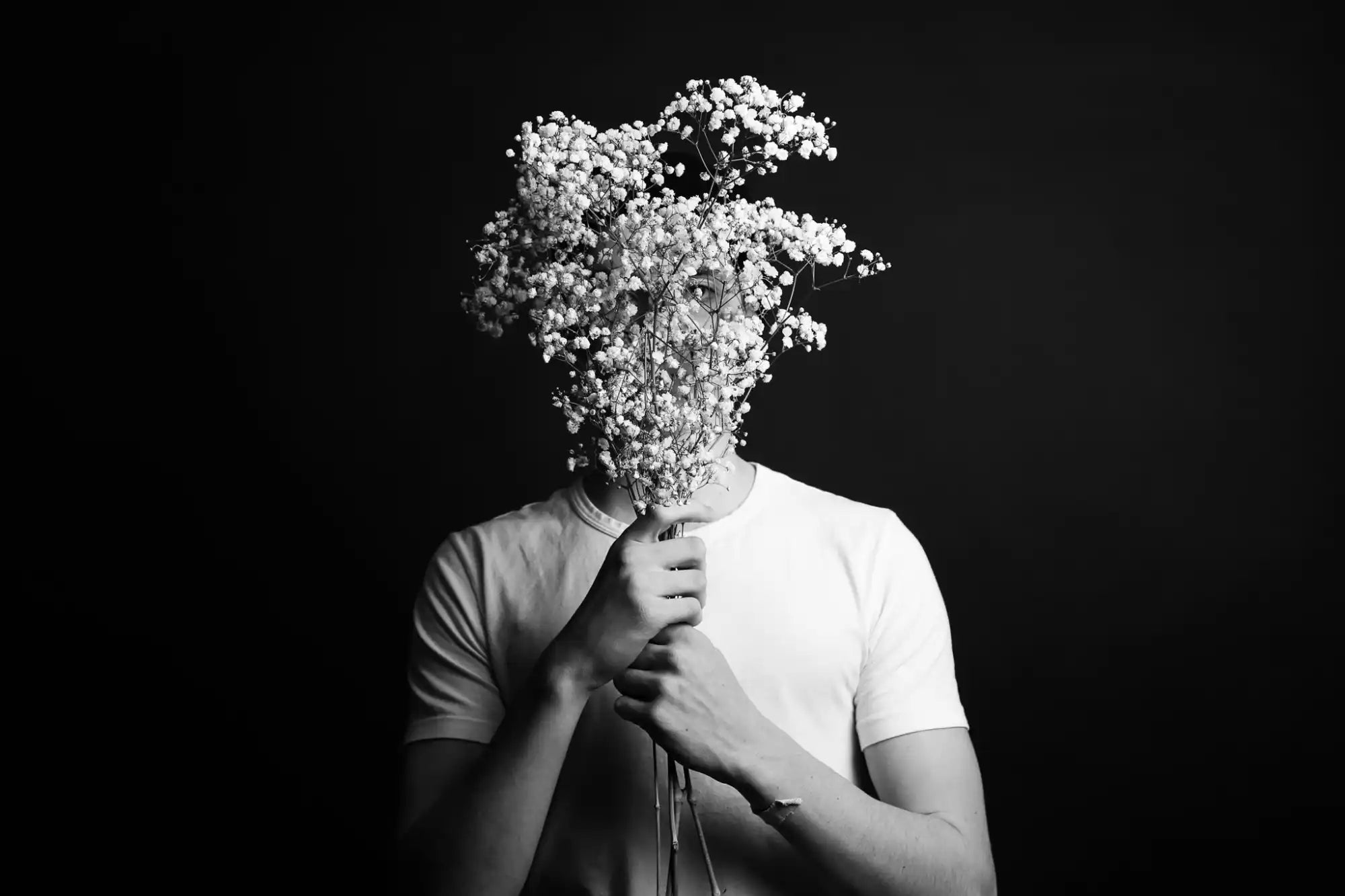 Des fleurs de souffle de bébé blanc tenues devant l'endroit où se trouverait un visage.