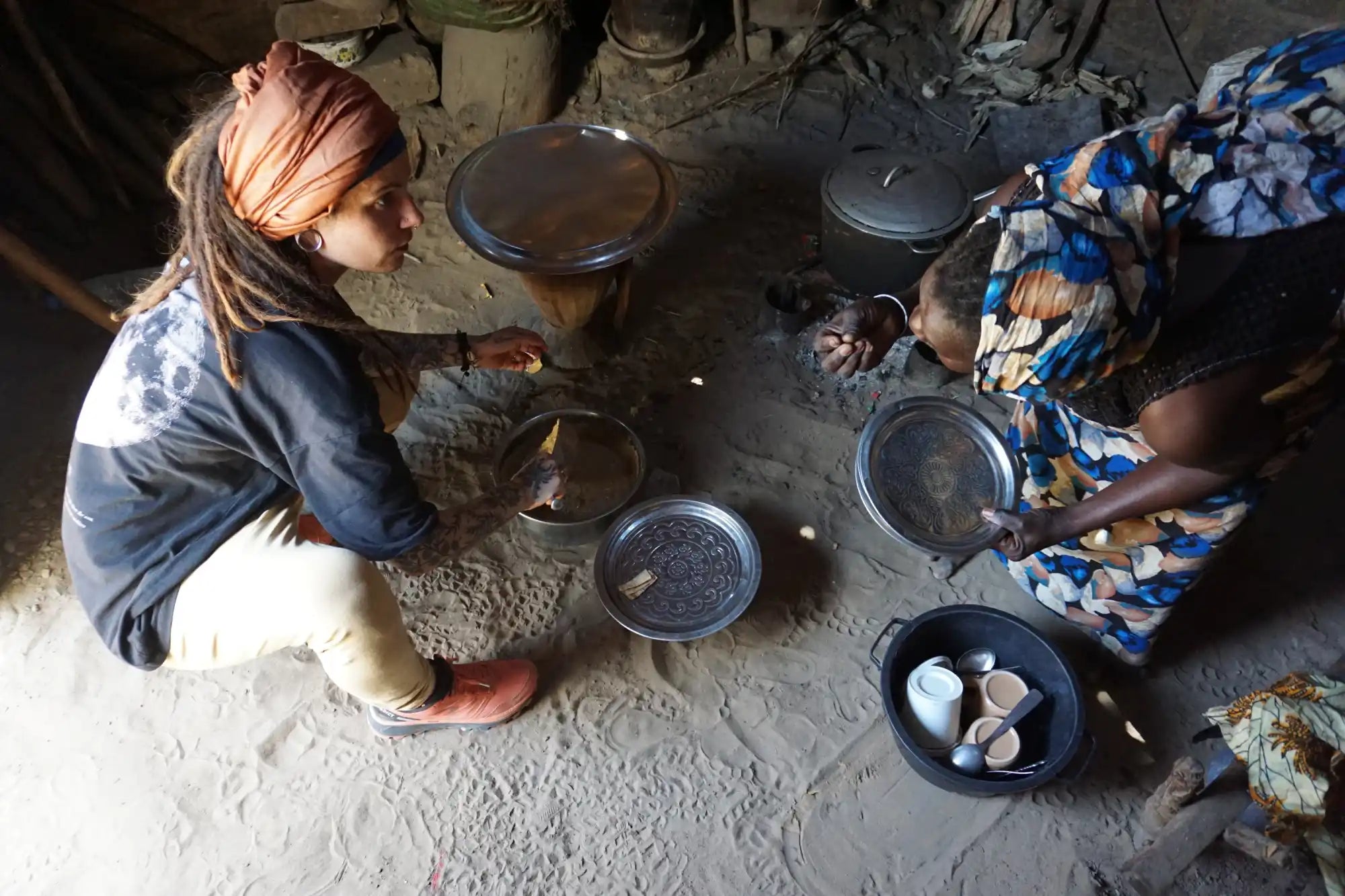 Des personnes préparant ou cuisinant de la nourriture assises par terre avec plusieurs assiettes et plats autour d'eux.